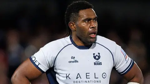 Viliame Mata stands with his hands on his hips