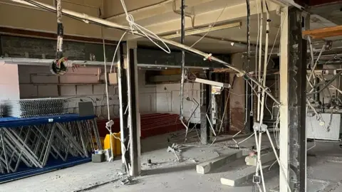 John Devine/BBC The inside of the Ploughmans pub in Werrington which has been closed and the inside has been gutted. Exposed wires and parts of the ceiling are in the picture. 