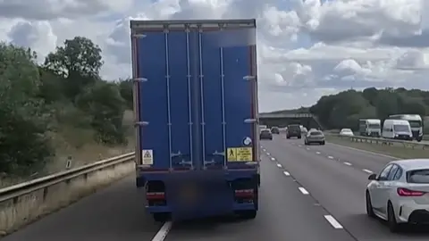 A blue lorry swerving into the hard shoulder lane on a motorway.