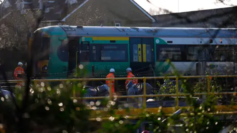 PA Media A train seen from behind a fence, with engineers standing next to it