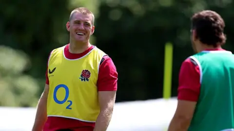 Getty Images Alex Coles looking at a teammate and smiling. He is wearing a red top with a hi-vis yellow bib over the top.