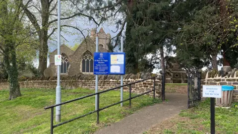 Tony Fisher/BBC The front of a church with a path leading up to it. The blue sign outside reads: "Welcome to St Mary the Virgin, Maulden".