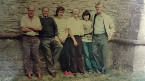John Gibson A very old, faded, photo of six bell ringers standing outside by a church tower in casual clothes and smiling to camera