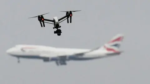 PA Media A drone in the foreground positioned in the photograph over a large British Airways jet aircraft out of focus in the background. 