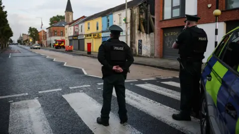 Two police officers look up a street with their backs to the camera