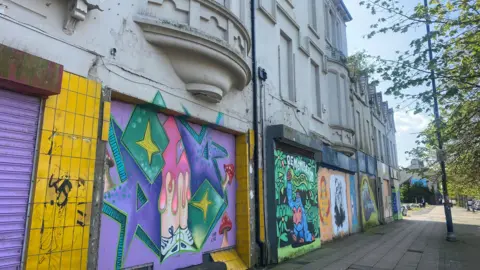 A row of empty shop units with graffiti on their shutters.