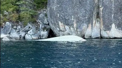 The white boat seen upside down floating near rocks
