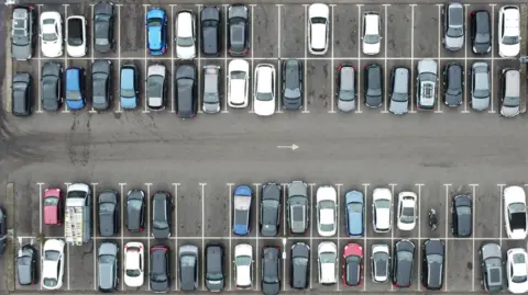 Overhead aerial view of a car park full with cars.