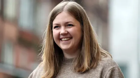 Getty Images Gillian Mackay, who has shoulder length fair hair, smiles while walking on a street 
