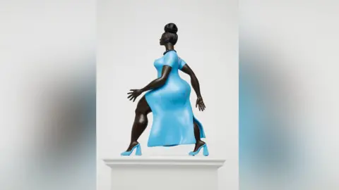 A statue of a woman of colour wearing a striking baby blue dress with matching high heels of the same colour. She has her hair up in a bun and is wearing a black beaded necklace. She is walking with purpose with one arm in front of the other.