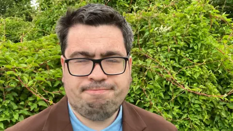 Guy Campbell/BBC Lib Dem candidate wearing glasses and a brown jacket