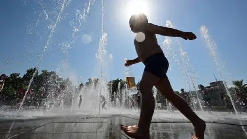 Getty Images A stock image showing a young boy running through water fountains on a bright sunny day. 