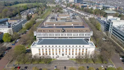 Getty Images an aerial view of a large greco roman inspired building in front of a larger 1960's style brutalist building stretching into the distance with north road cardiff and bute park visible
