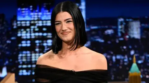 Getty Images A woman with straight black hair smiles. She is in the studio of the Jimmy Fallon show.