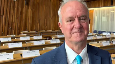 Martin Griffiths in a blue suit and tie inside a wooden panelled council chamber.