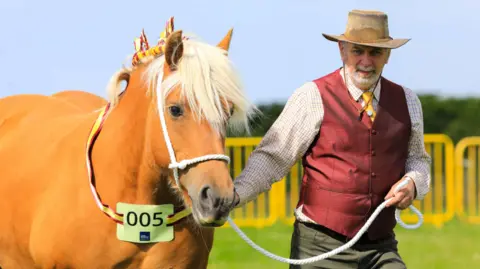 CJS Photography A man, wearing a cowboy hat, leading a golden horse, with blonde hair