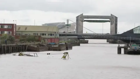 A view of the River Hull looking towards the city's tidal barrier. The top of a crane barge is just visible through the surface of the water.