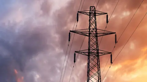 A British Style Electricity Pylon and suspended electic cables against a Blue Cloudy Sky