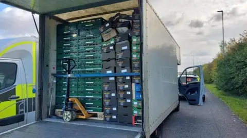 CAMBRIDGESHIRE POLICE A van is opened at the back which is showing boxes stacked up inside. The driver's door, on the right hand side, is open. 