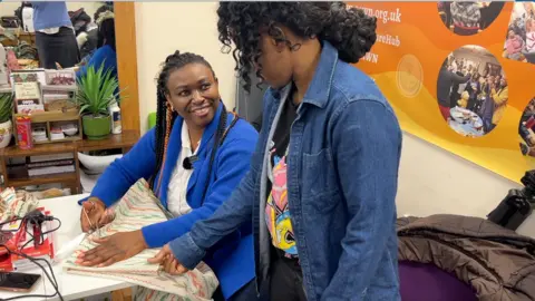 Kaya Black/ BBC News A woman smiling cutting some fabric