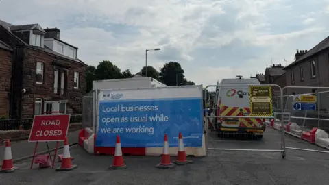 A street with building works going on. A sign says "local businesses open as usual while we are working"