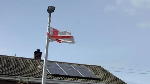BBC A St George's flag on a lamppost. In the background is the roof of a house with a solar panel on it