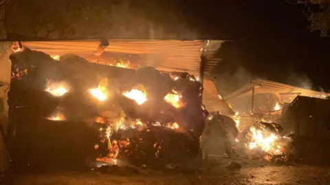 A nighttime picture showing hay bales and a metal outbuilding on fire.