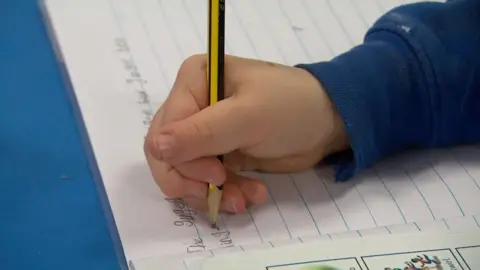 A child's hand writing in a school exercise book.
