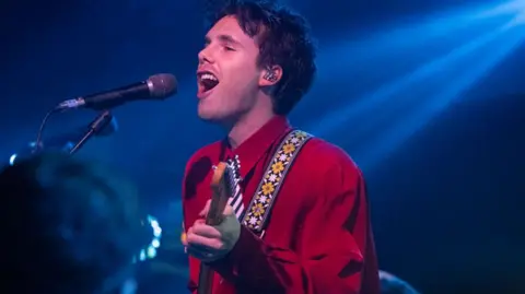 Cruz singing and playing the guitar 