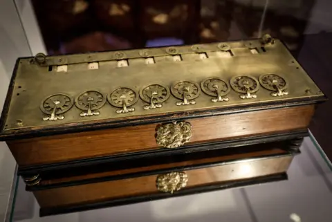 AFP via Getty Images Close-up of La Pascaline, a brass wooden box accented with a line of small metallic wheels on top.