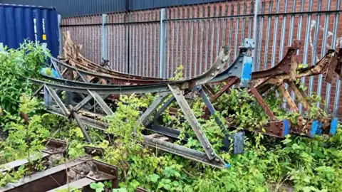 Severn Valley Railway A pile of metal girders in an overgrown area with a corrugated metal fence behind it