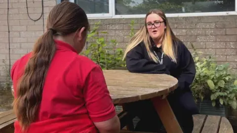 Nevaeh talking to a girl while they sit at a bench