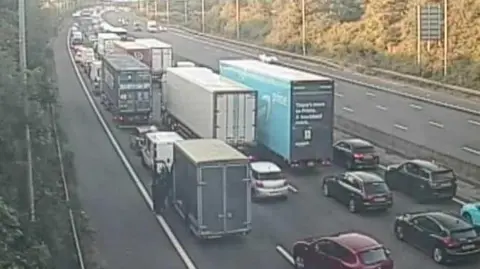 National Highways A traffic camera showing a four-lane motorway full of cars at a stand still.