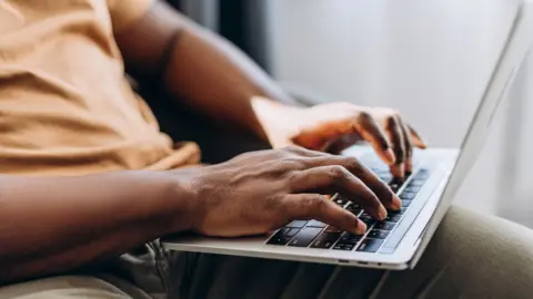 Stock photo shows a close up image of someone typing on a laptop while stiiting at home.