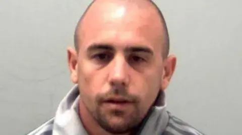 Essex Police A custody picture of Ben Ransome, who has a shaved head and stubble. He looks resigned and is wearing a grey Adidas jumper.