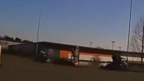 Supplied A still from dashcam footage showing a road junction on an industrial estate with a red convertible car stationary and a figure standing on the bonnet