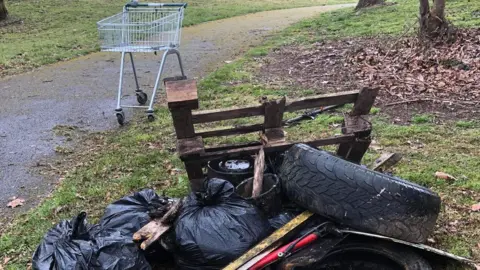 Gavin Cox Fly-tipped waste by the side of a path in a par. Full black bin bags, tyres, a pallet and buckets and a stray shopping trolley have all been left abandoned.