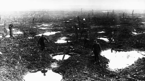 Getty Images Soldiers walk around puddles created by bombing on the wetlands near Gheluvelt. The image is black and white and features tree trunks that have been bombed 