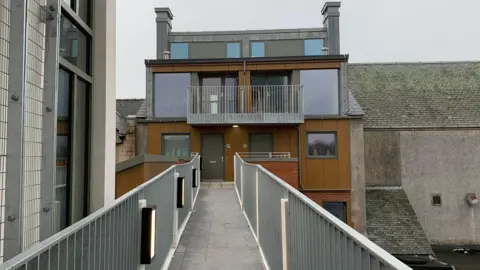 A modern apartment building at the top of a redevelopment with a pathway leading up to it between railings