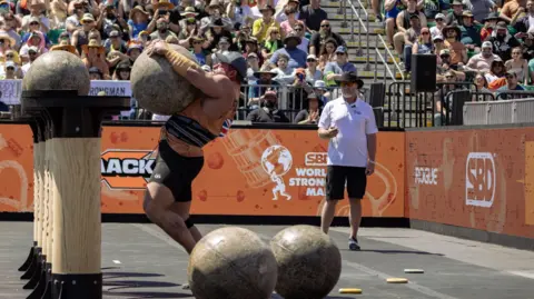 World's Strongest Man Shane Flowers lifting a heavy stone at the worlds strongest man event in front of crowds