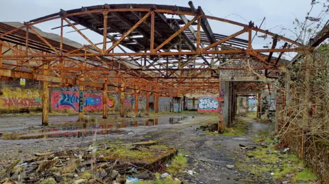 Loch Lomond & The Trossachs National Park Authority A disused military station, that has been out of use for decades. Overgrown greenery covers parts of it, while graffiti is all over the walls and many pillars and infrastructure of the building are rusting. 