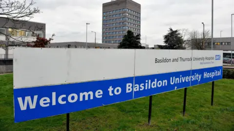 PA A blue and white hospital sign that reads: "Welcome to Basildon University Hospital". Behind the sign is a high-rise brutalist building. 