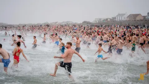 John Ross Photography Hundreds of people run into the sea.
