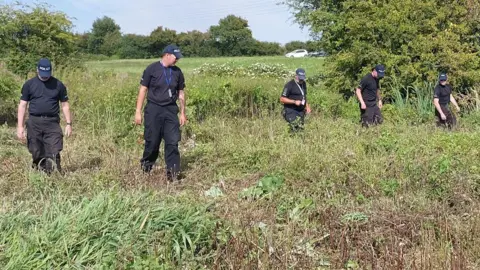 Essex Police Several police officers wearing all black walking in a field.