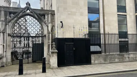 Black-painted, wooden boxing with a locked doorway around a section of wall of the Royal Courts of Justice, which was painted with a mural by Banksy.