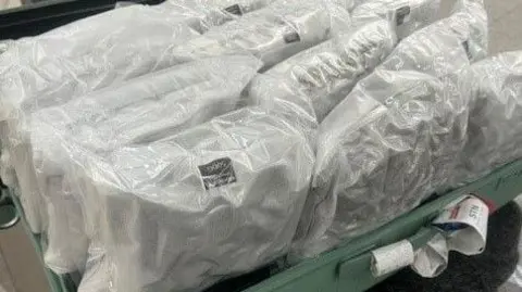NCA A bundle of vacuum packed white plastic bags full of cannabis, loaded into a green suitcase.