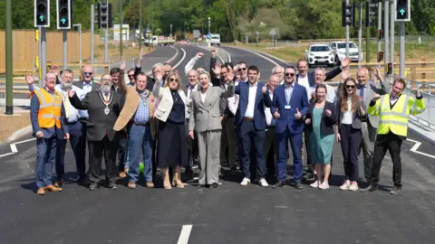 Eddie Mitchell / West Sussex County Council A group of people stood in the middle of a road. They are holding their hands up and holding their thumbs up to the camera while smiling.
