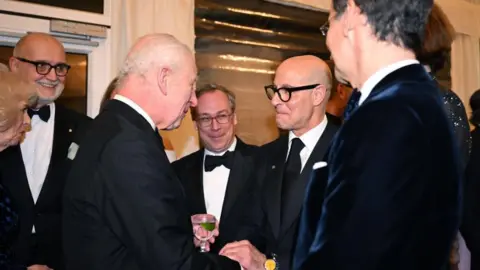 Getty Images King Charles shakes Stanley Tucci's hands at a black-tie event.