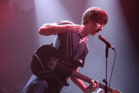 Arctic Monkeys frontman Alex TurnerArctic Monkeys frontman Alex Turner singing into a mic while strumming his guitar