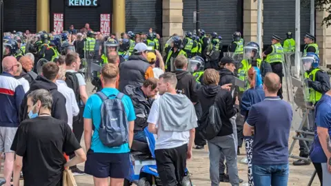  @funky_nelli Crowds of people standing in front of police officers holding riot protection gear